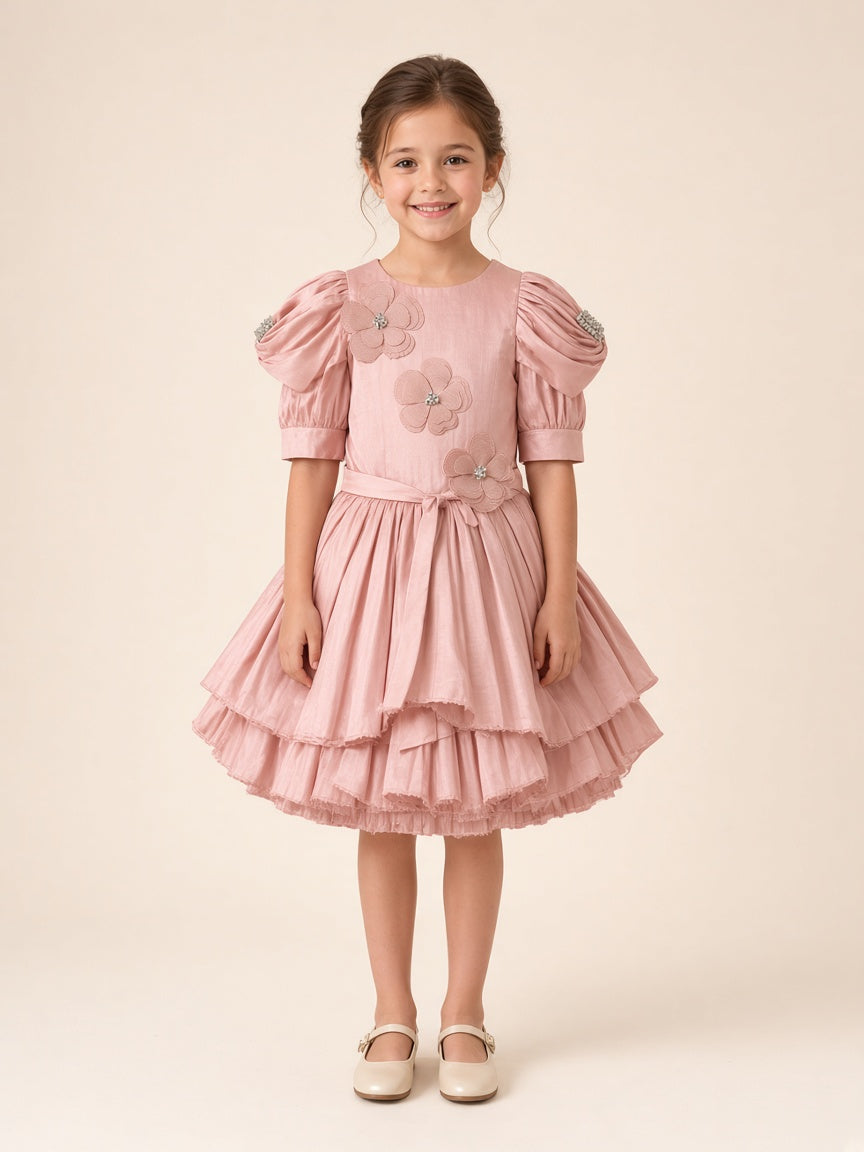 Girl wearing dusty pink floral appliqué party frock with puff sleeves and rhinestone sleeve band